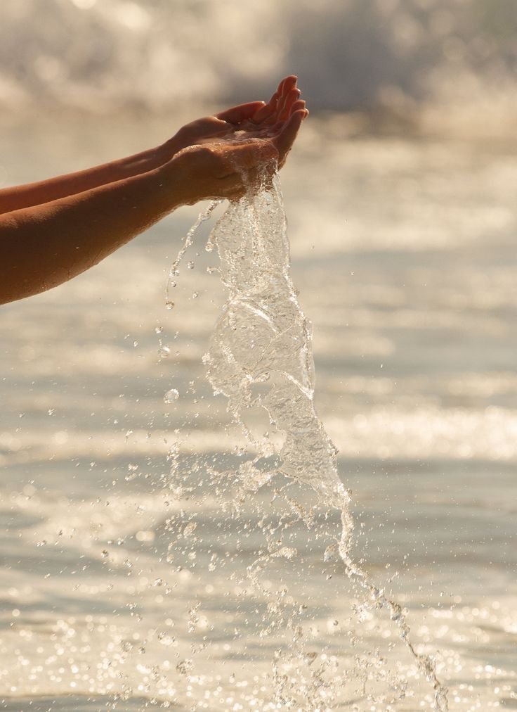 Hands playing with water in the ocean at sunset