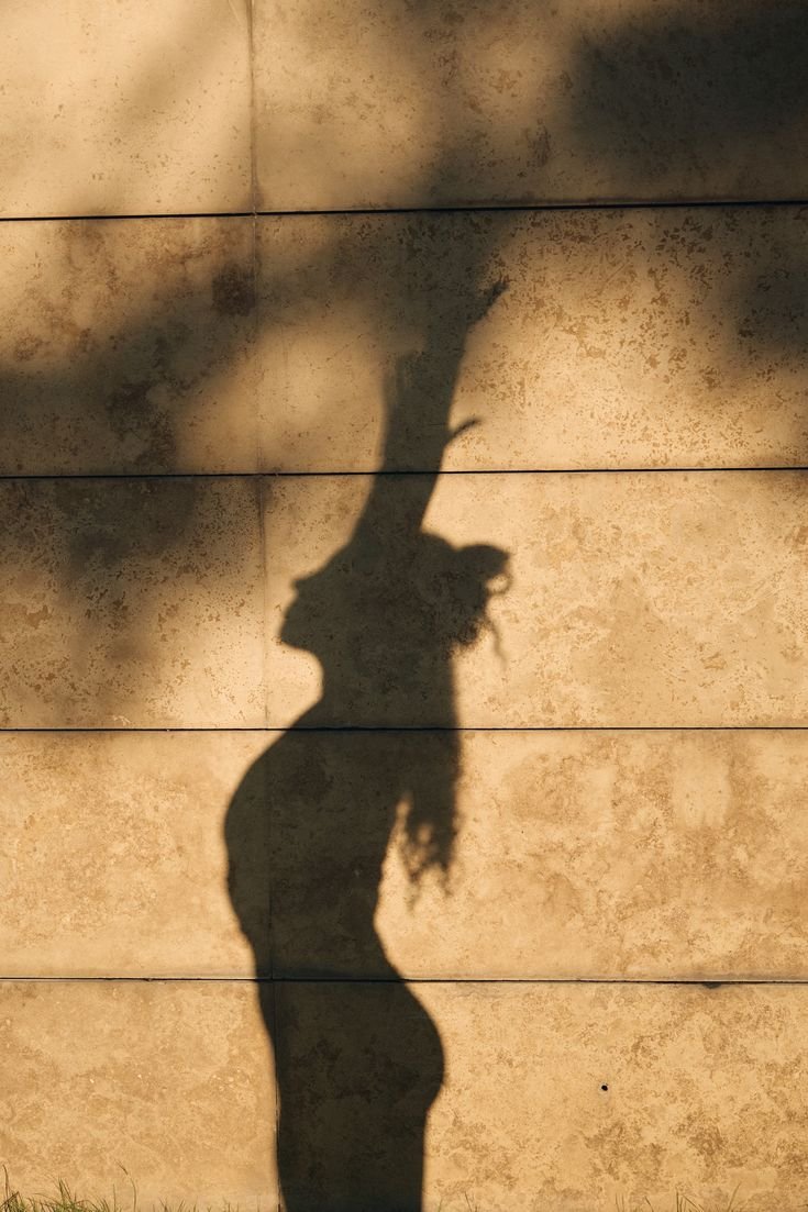 Shadow of a woman with curly hair cast on a beige tiled wall.