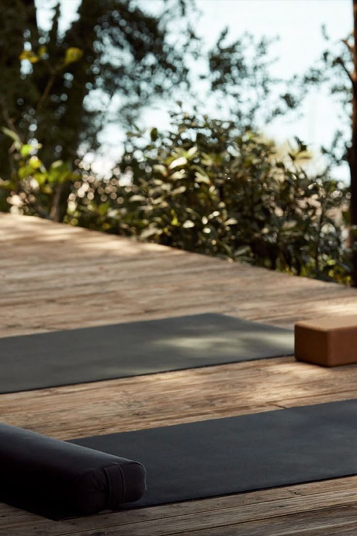 Yoga mats and blocks set up outdoors on wooden decking surrounded by trees.