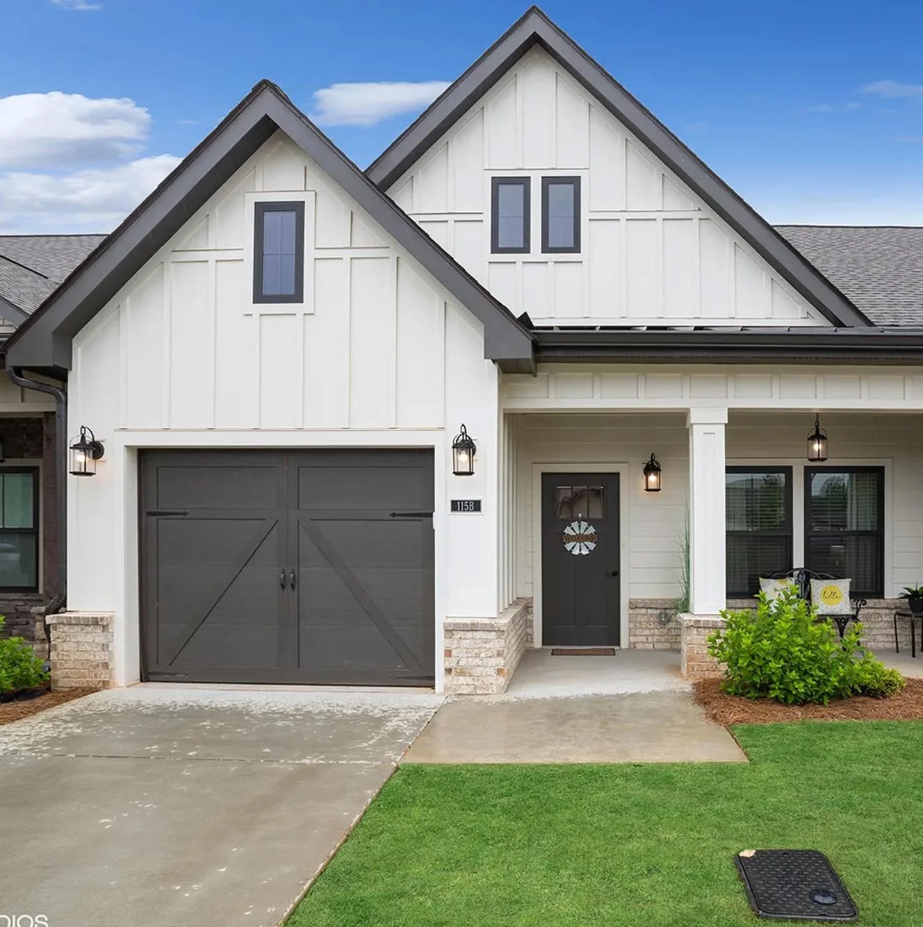 Front view of a modern cottage at The Phoenix at Dallas, with white siding, black garage door, front door with wreath, porch lighting, and a well-maintained lawn.