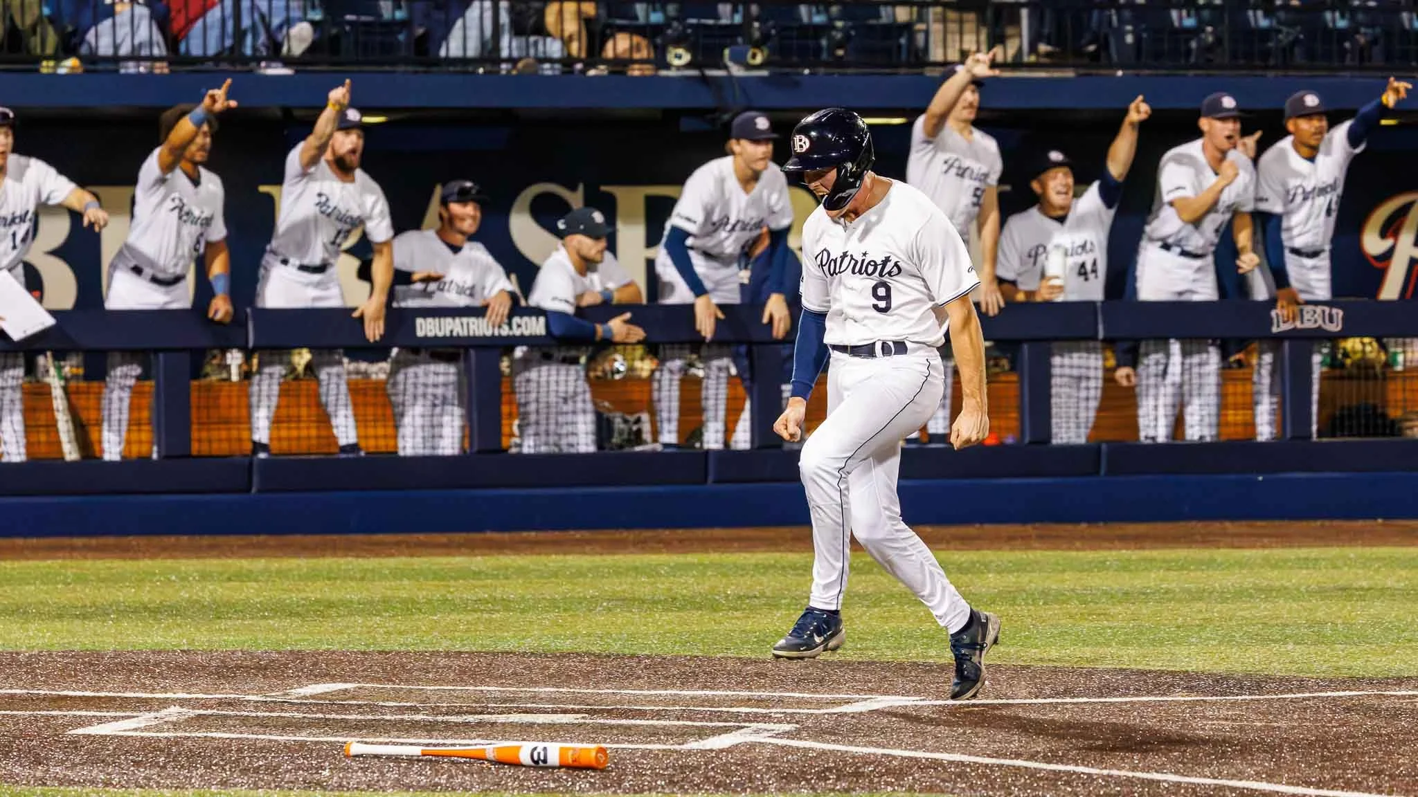 Dallas Baptist Patriots player number 9 celebrates in front of the dugout while scoring during NCAA Division I baseball game at Horner Ballpark.