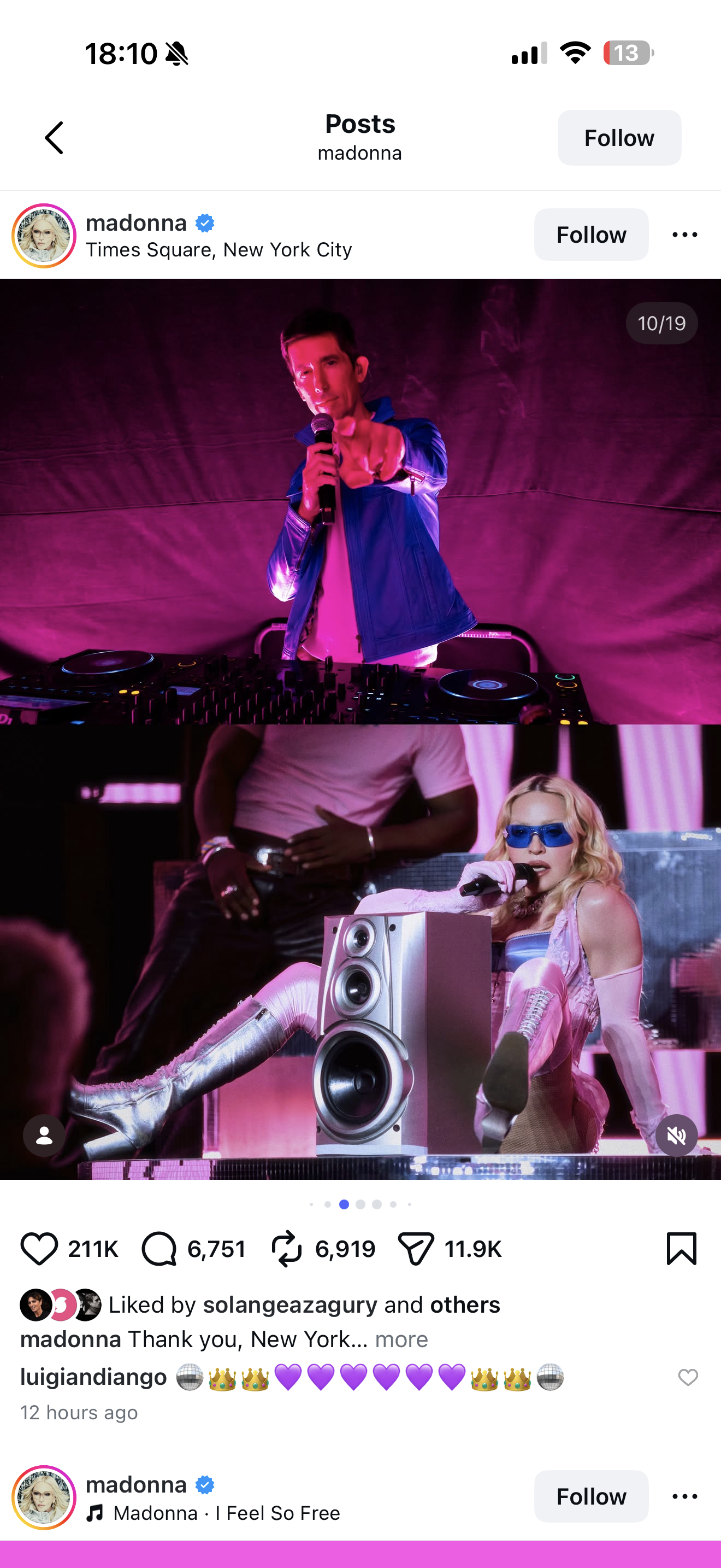 Madonna performing at a concert in Times Square, New York City, with vibrant pink and purple lighting. She is seated on the stage, wearing metallic silver boots and pink outfit, with bright blue sunglasses, holding a microphone. A DJ is standing behind her, and a DJ equipment setup is visible.