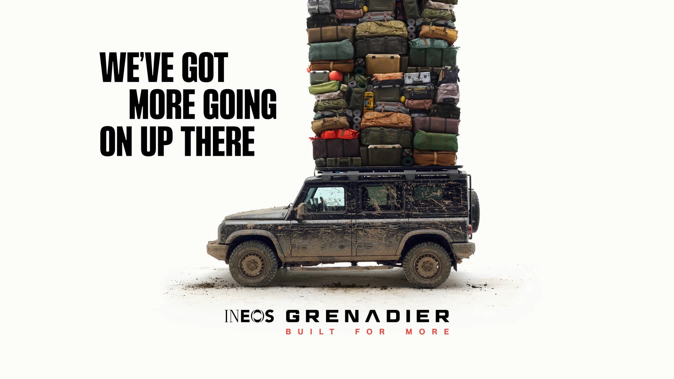 A black off-road vehicle piled high with camping and outdoor gear, such as tents and backpacks, with the text 'We've got more going on up there' and 'INEOS Grenadier Built for More' on a white background.