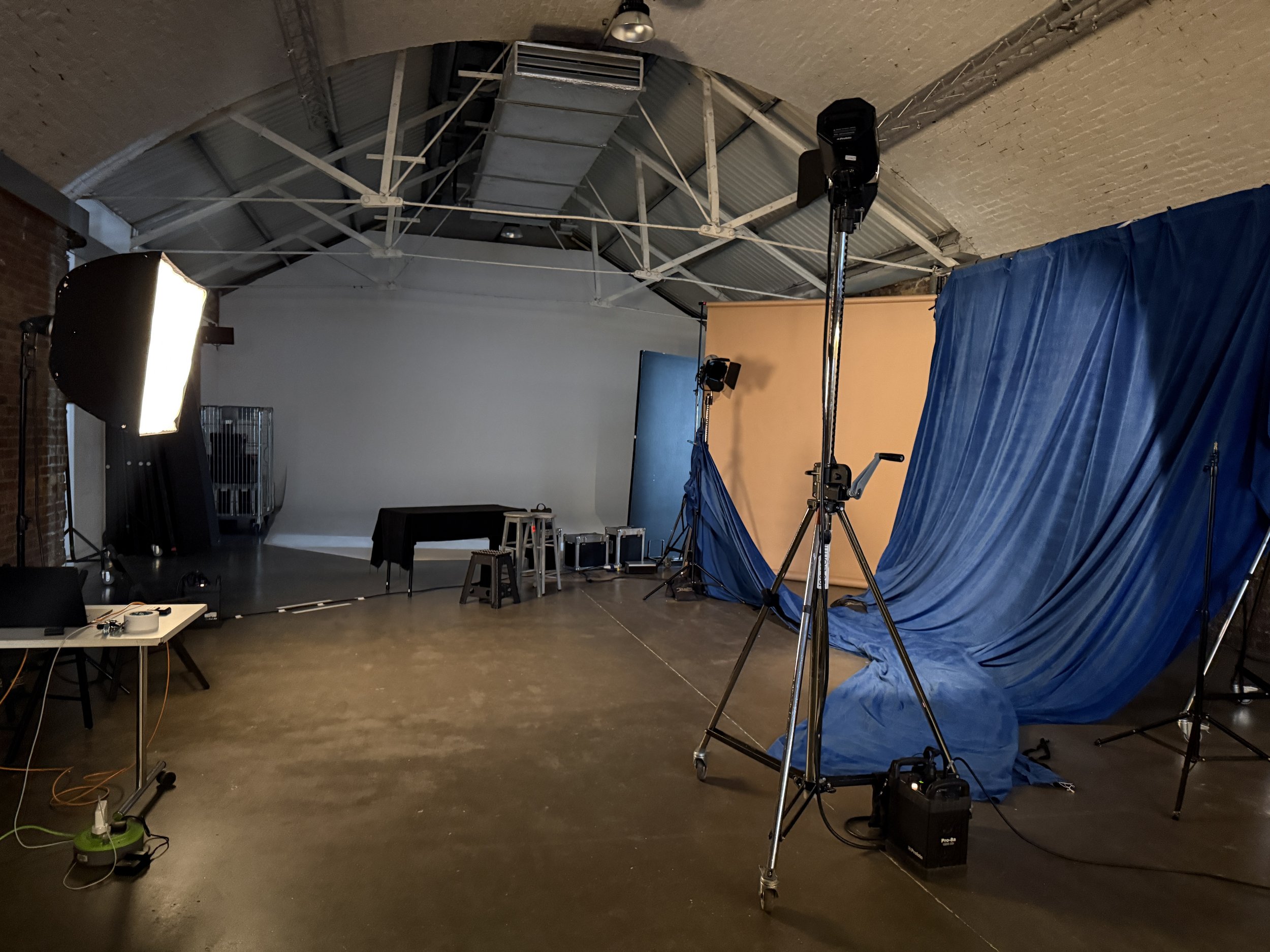 A photography studio setup with professional lighting, a blue curtain, a yellow backdrop, tripods, and various equipment inside a space with a vaulted ceiling and exposed brick walls.