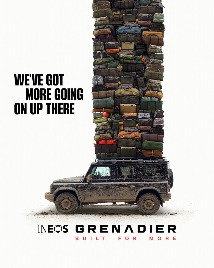 A black, muddy vehicle with a tall stack of various bags and equipment on top, along with the text 'We've got more going on up there' and 'INEOS Grenadier Built for More'.