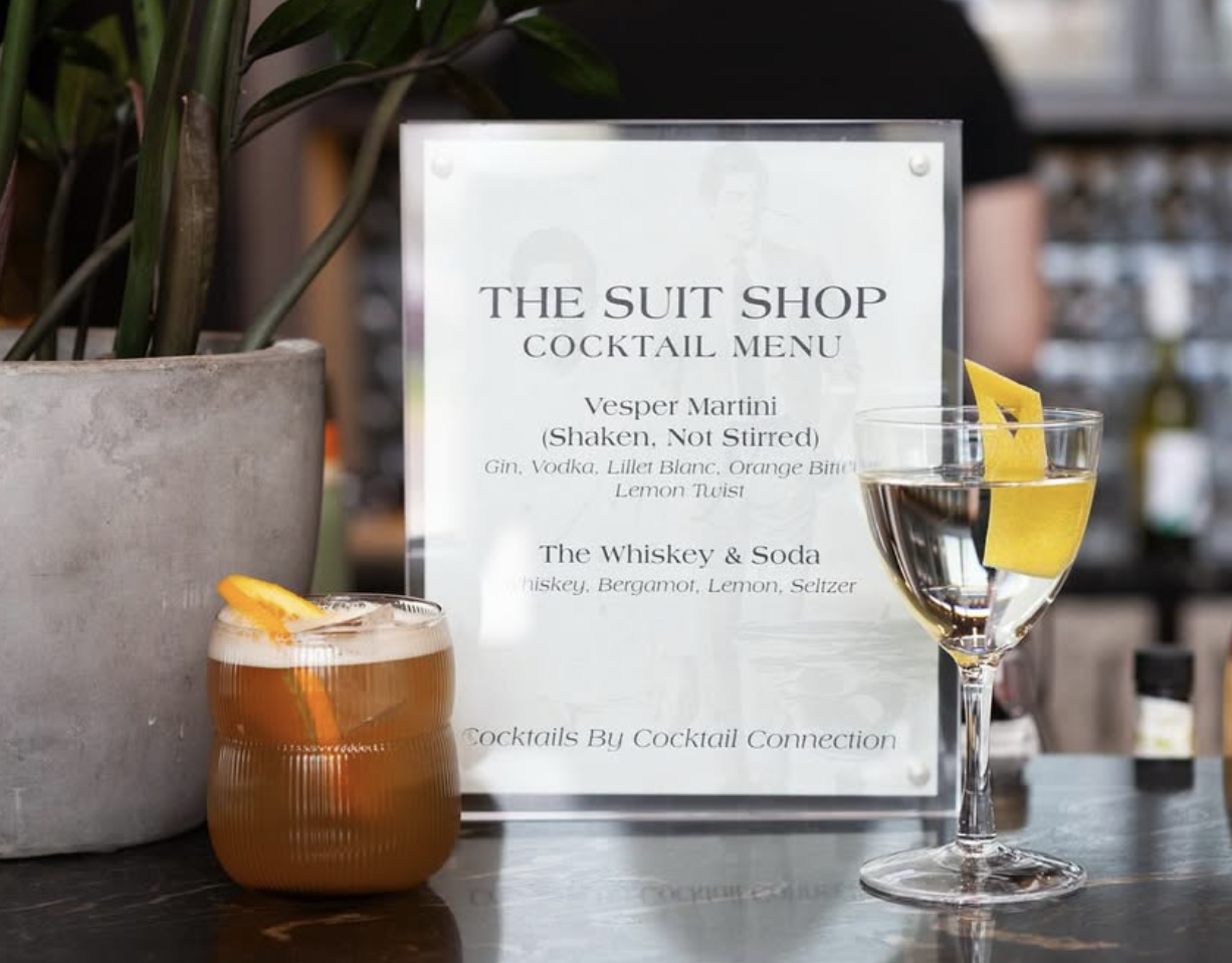 Cocktail drinks on a bar counter with a cocktail menu sign in the background.