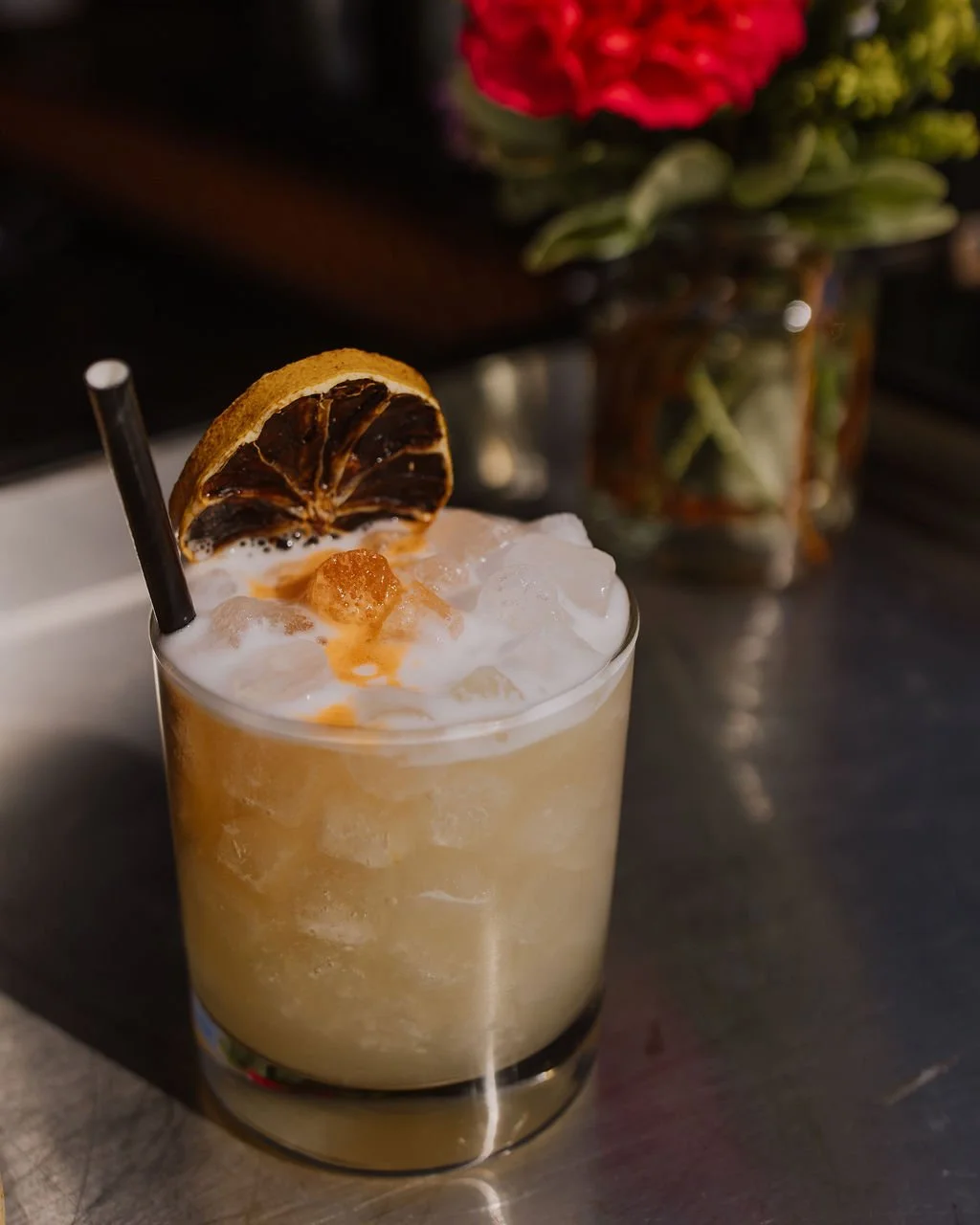 Creamy cocktail in a glass garnished with a dried citrus slice and foam, with a black straw.
