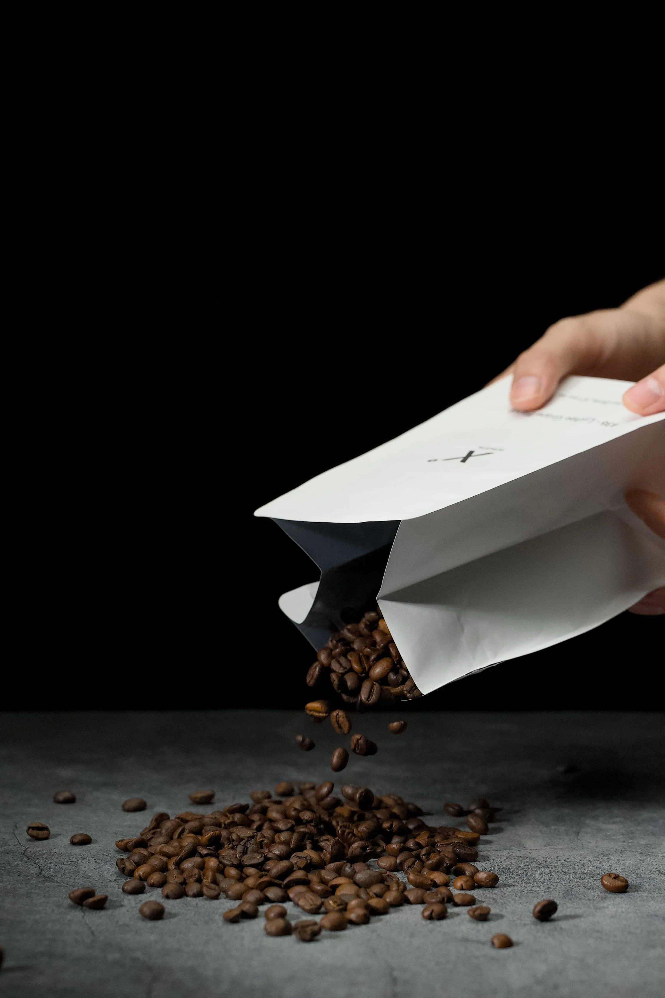 Hand pouring X° Robusta coffee beans from a white bag onto a dark surface.