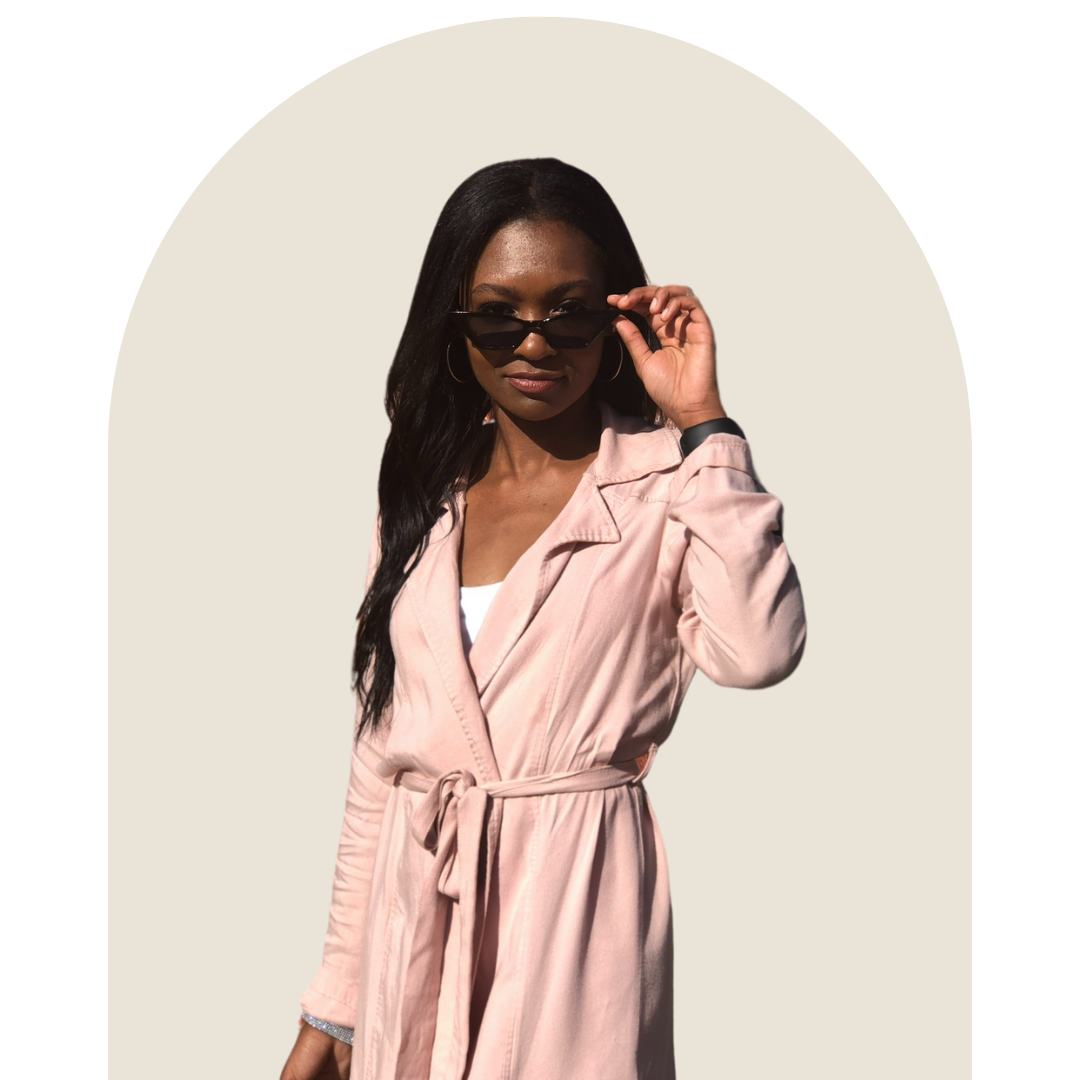 A woman wearing a light pink coat and sunglasses, adjusting the glasses with her right hand, against a neutral background.