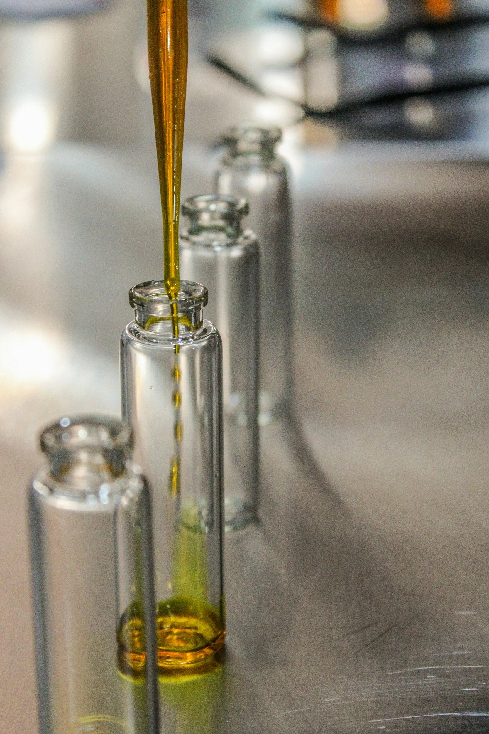 Close-up of liquid being poured from a pipette into small glass vials on a metallic surface.