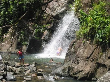 People enjoying a waterfall in a natural setting with rocks and greenery.