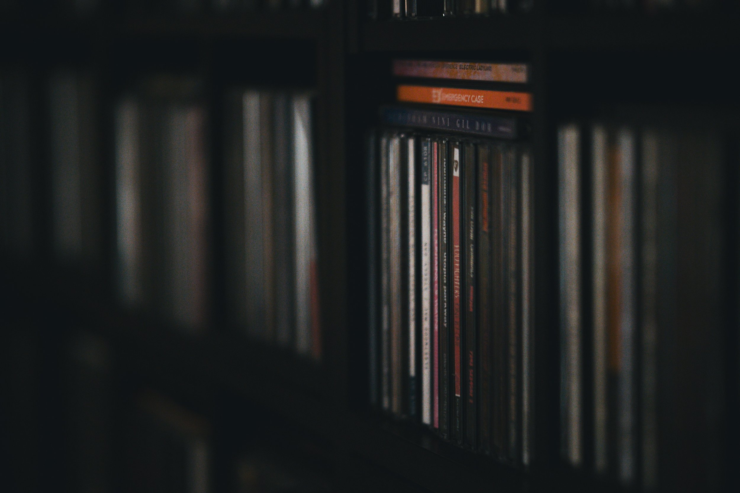 A dimly lit shelf filled with rows of compact discs (CDs), some with visible titles.
