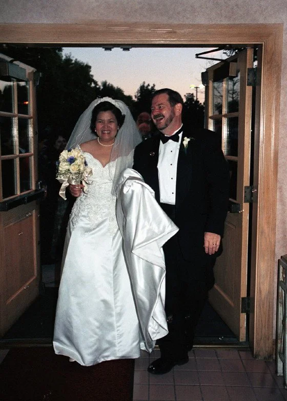 Bride and groom walking out of a building, the bride in a white dress holding a bouquet, and the groom in a black suit with a bow tie.