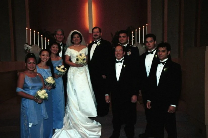 A wedding party posing for a group photo with people in formal attire, including the bride in a white gown and groom in a tuxedo.