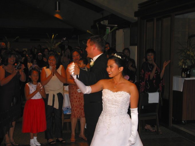 Bride and groom dancing at a wedding reception with guests clapping and watching.