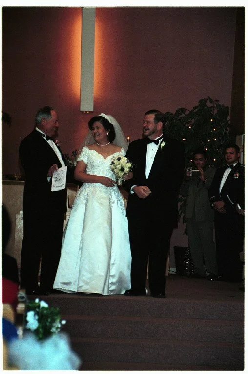 Bride and groom standing with officiant during wedding ceremony, indoor setting, bride holding bouquet.