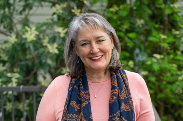 Woman smiling wearing a pink sweater and a navy scarf against a leafy background