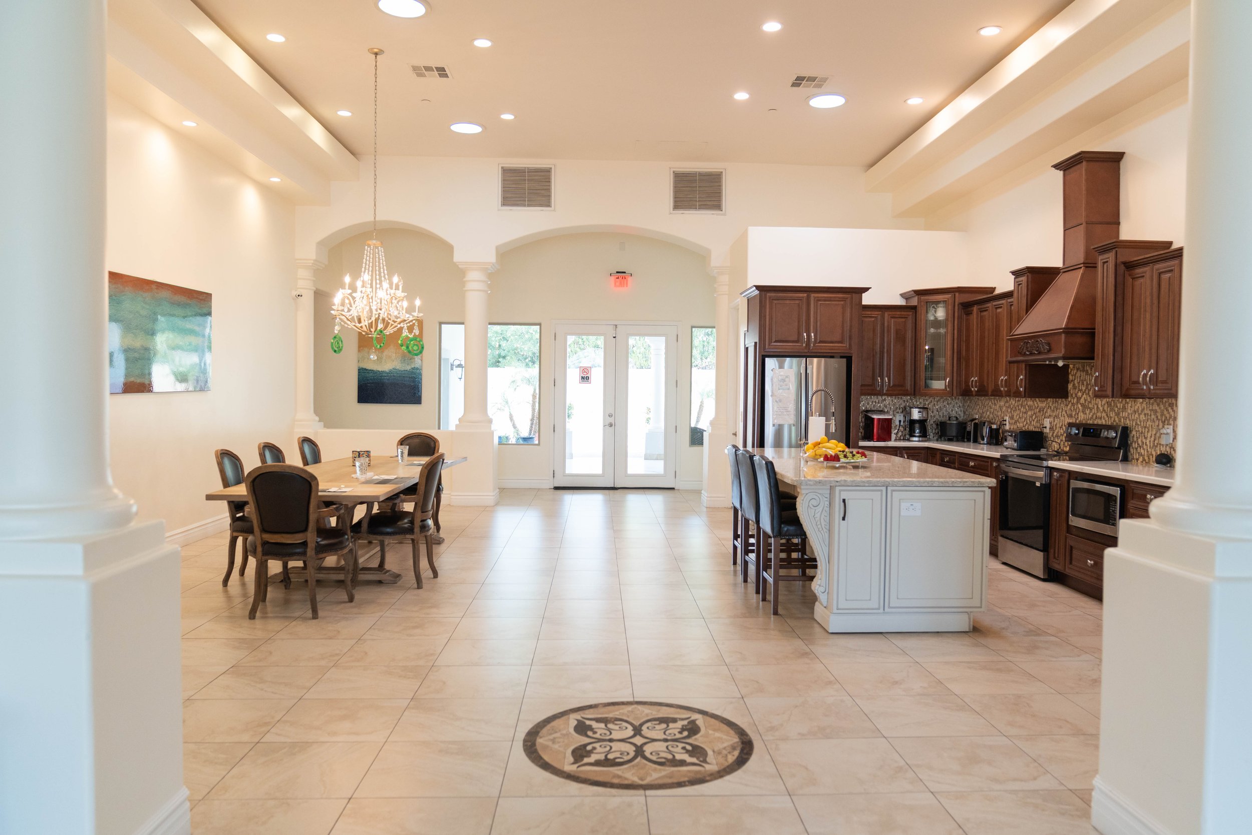 Modern kitchen with wooden cabinets and dining area featuring a chandelier and large windows.