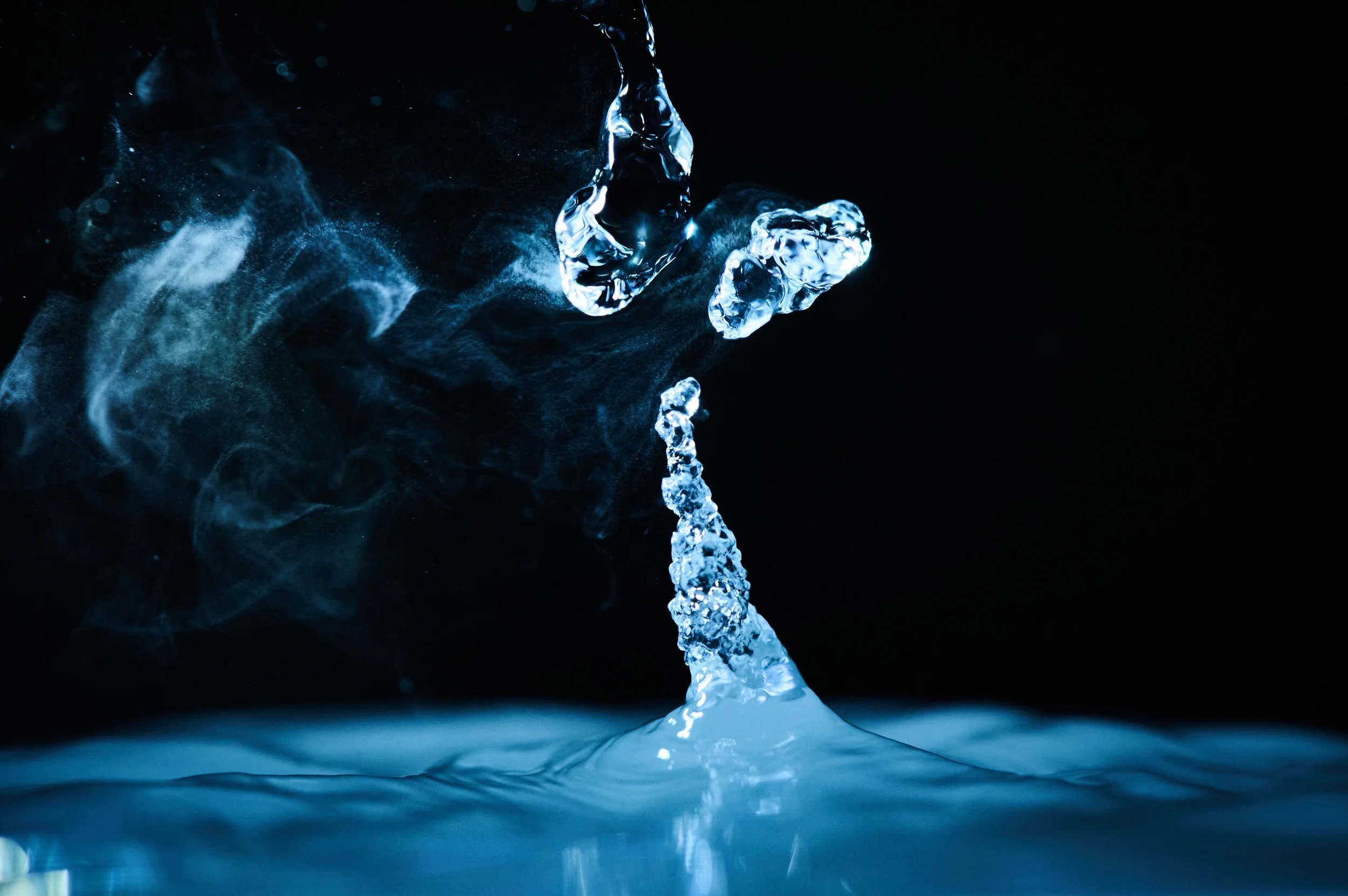 Close-up of water splash forming a column with droplets and mist against black background.