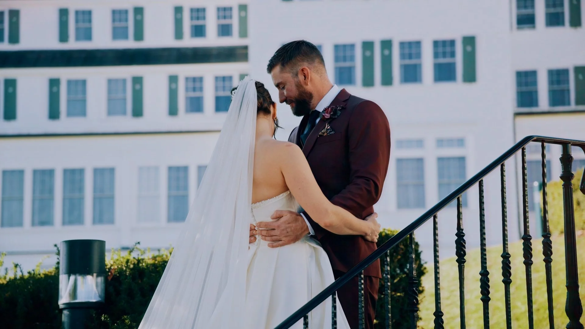 A bride and groom embrace during their wedding outside, with a tall building in the background.