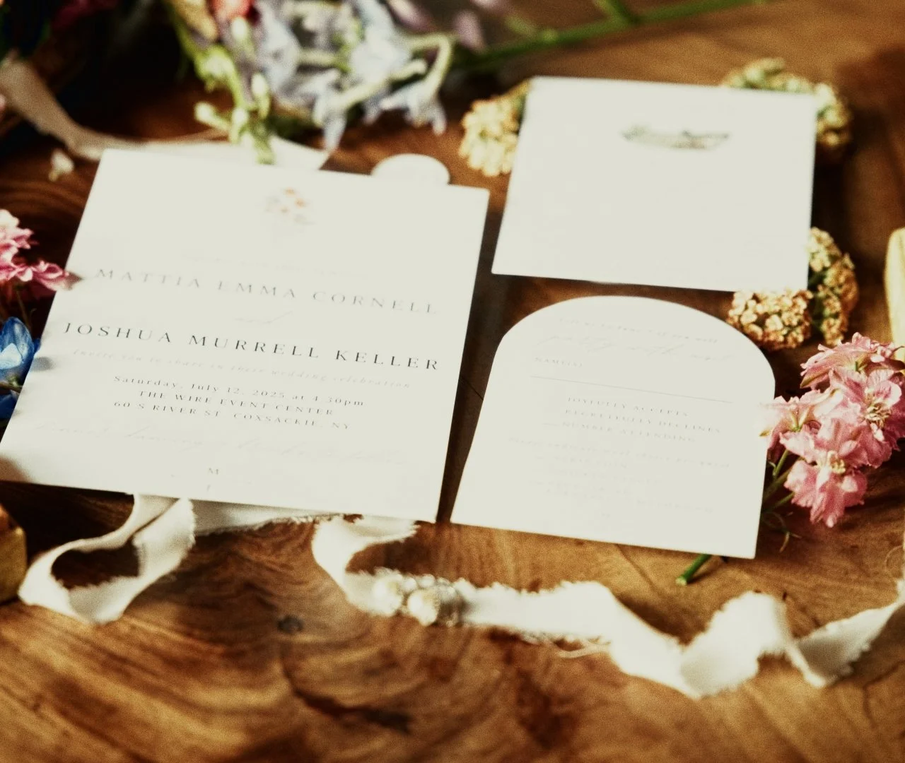 Wedding invitation cards placed on a wooden table surrounded by flowers and torn paper decorations.