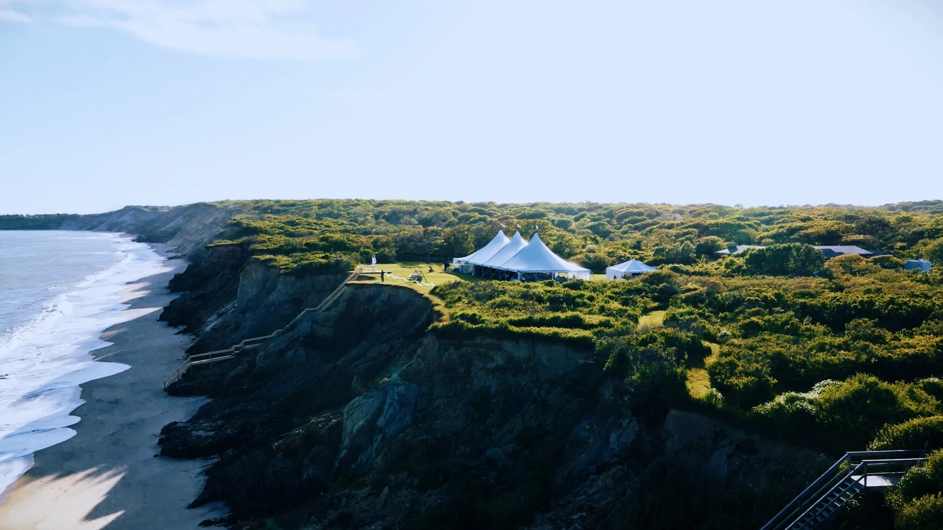 Tent set up on a grassy cliff overlooking the ocean on a sunny day.