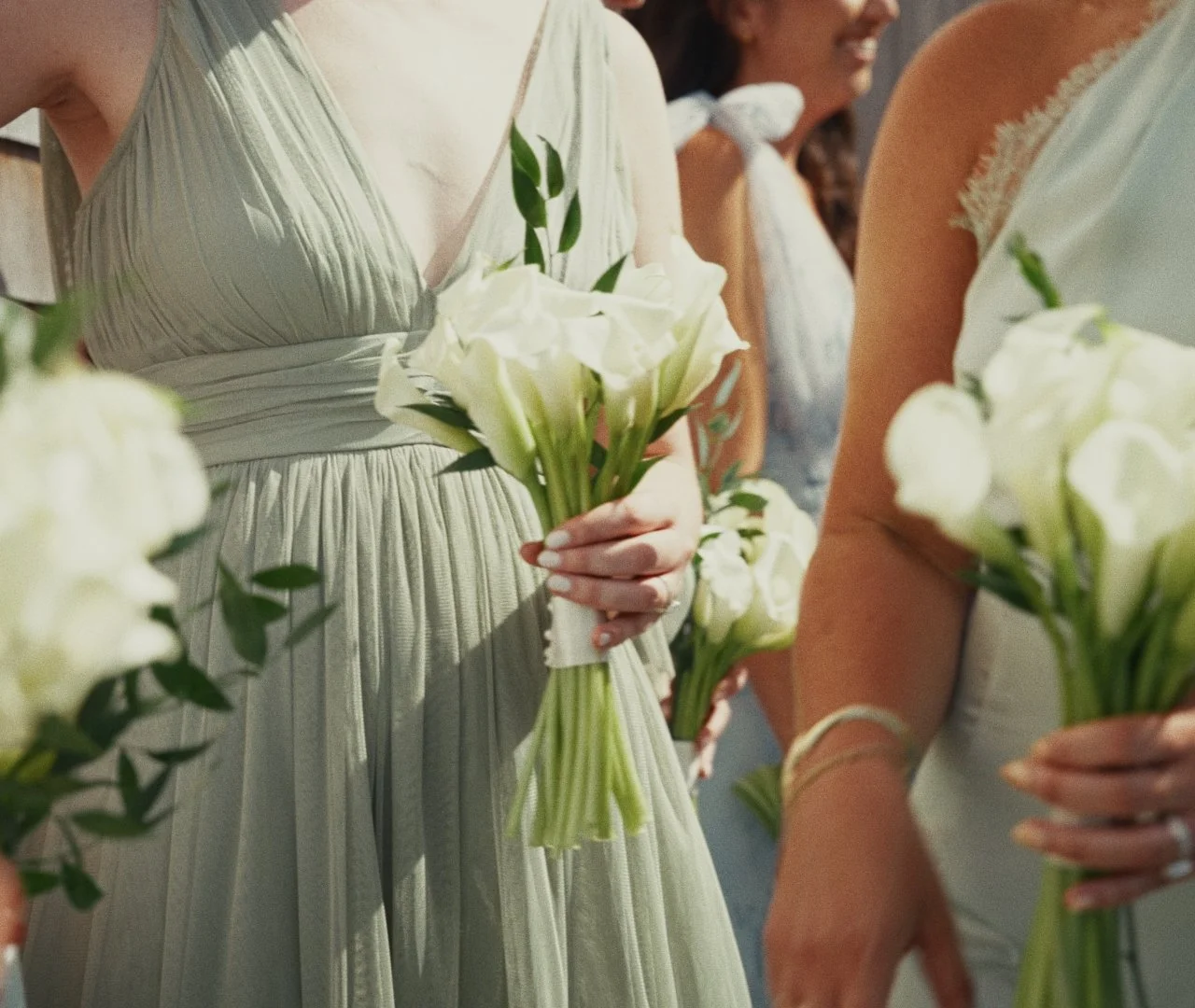 Women in formal attire holding bouquets of white flowers at a wedding ceremony.