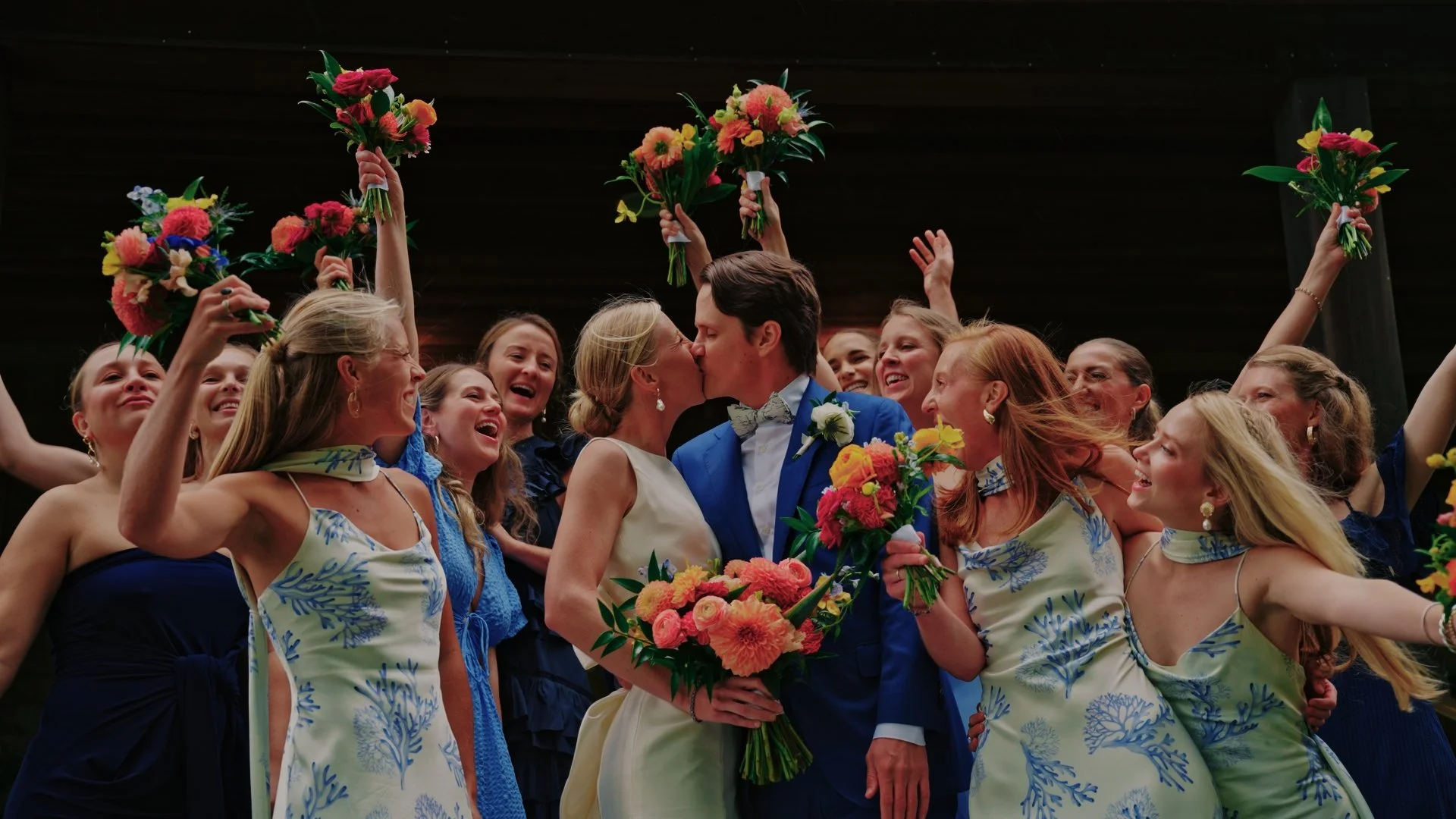 Wedding couple kissing surrounded by cheering women holding bouquets and celebrating