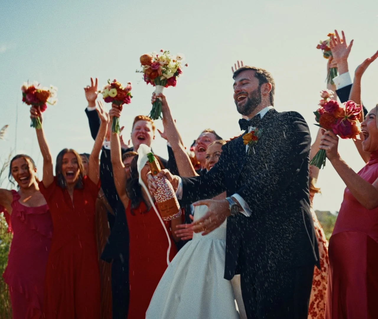 Celebrating newlyweds at a wedding with friends, fireworks, and flower bouquets outside.