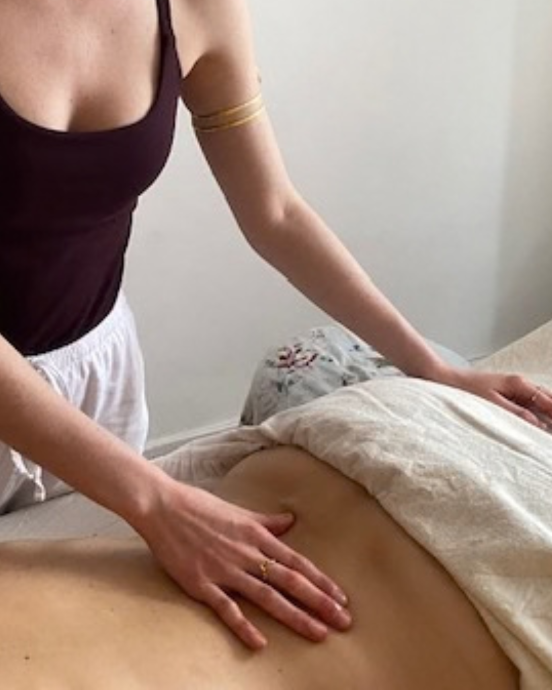 A woman giving a massage to a person lying face down on a bed, with the woman's hands on the person's lower back.