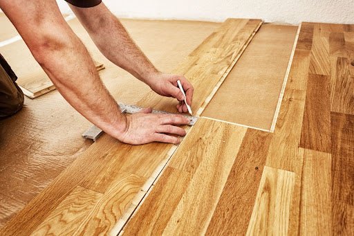Person installing hardwood floor planks, carefully aligning a new piece on the floor.