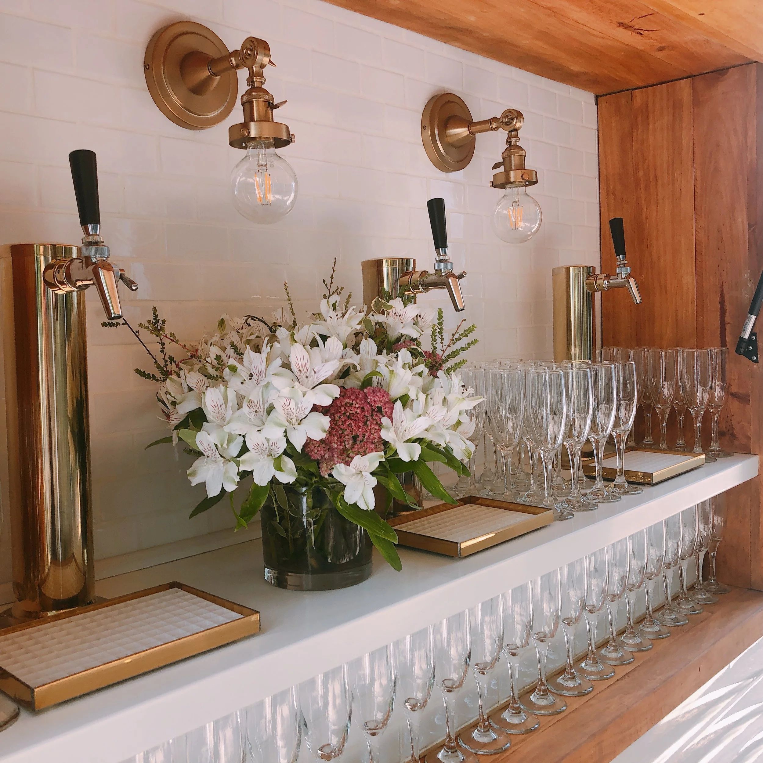 Bar with a floral centerpiece, glasses, and taps for serving beverages in a modern setting
