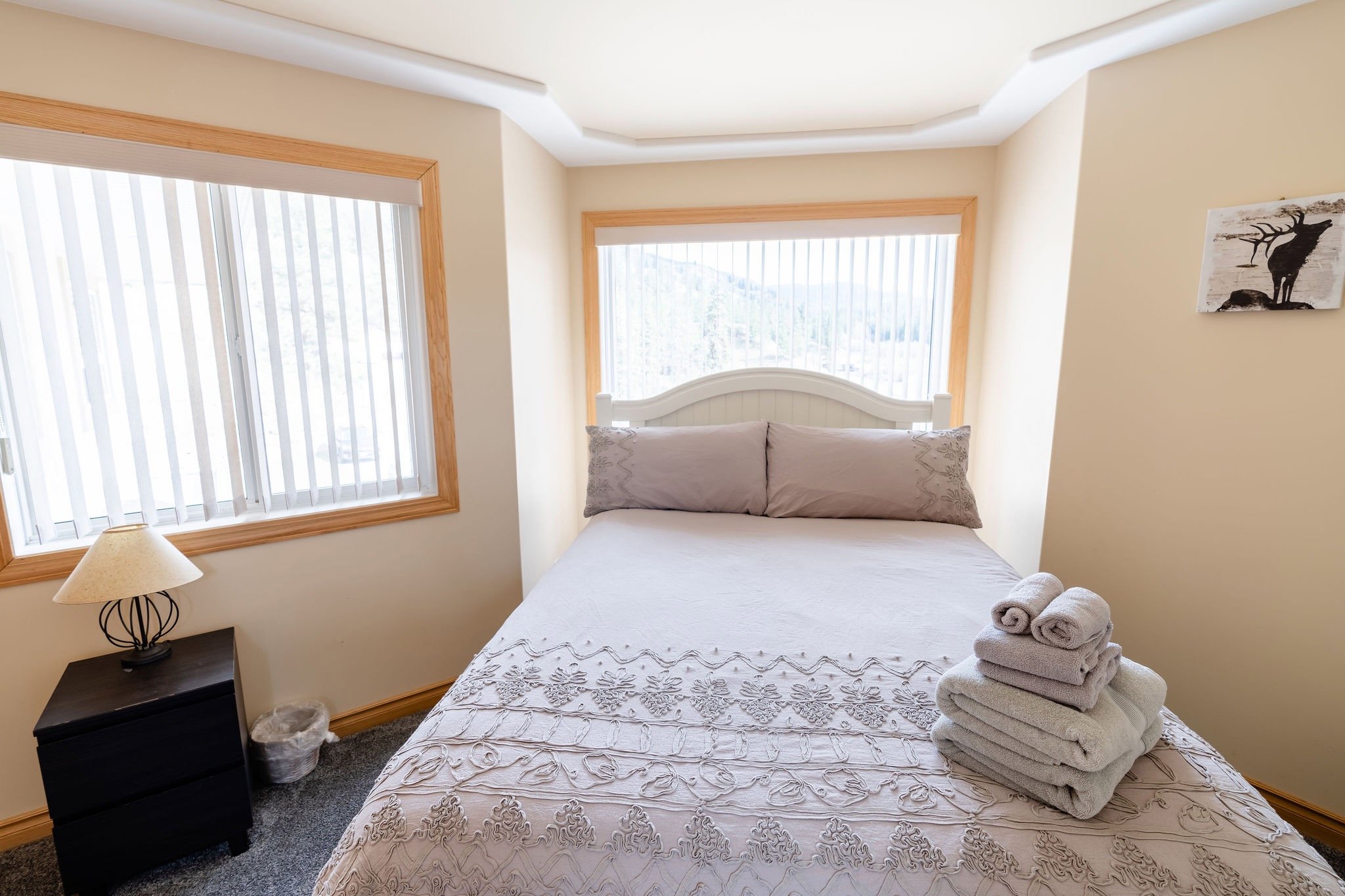 Clean bedroom with a bed, folded towels on it, and windows with vertical blinds.