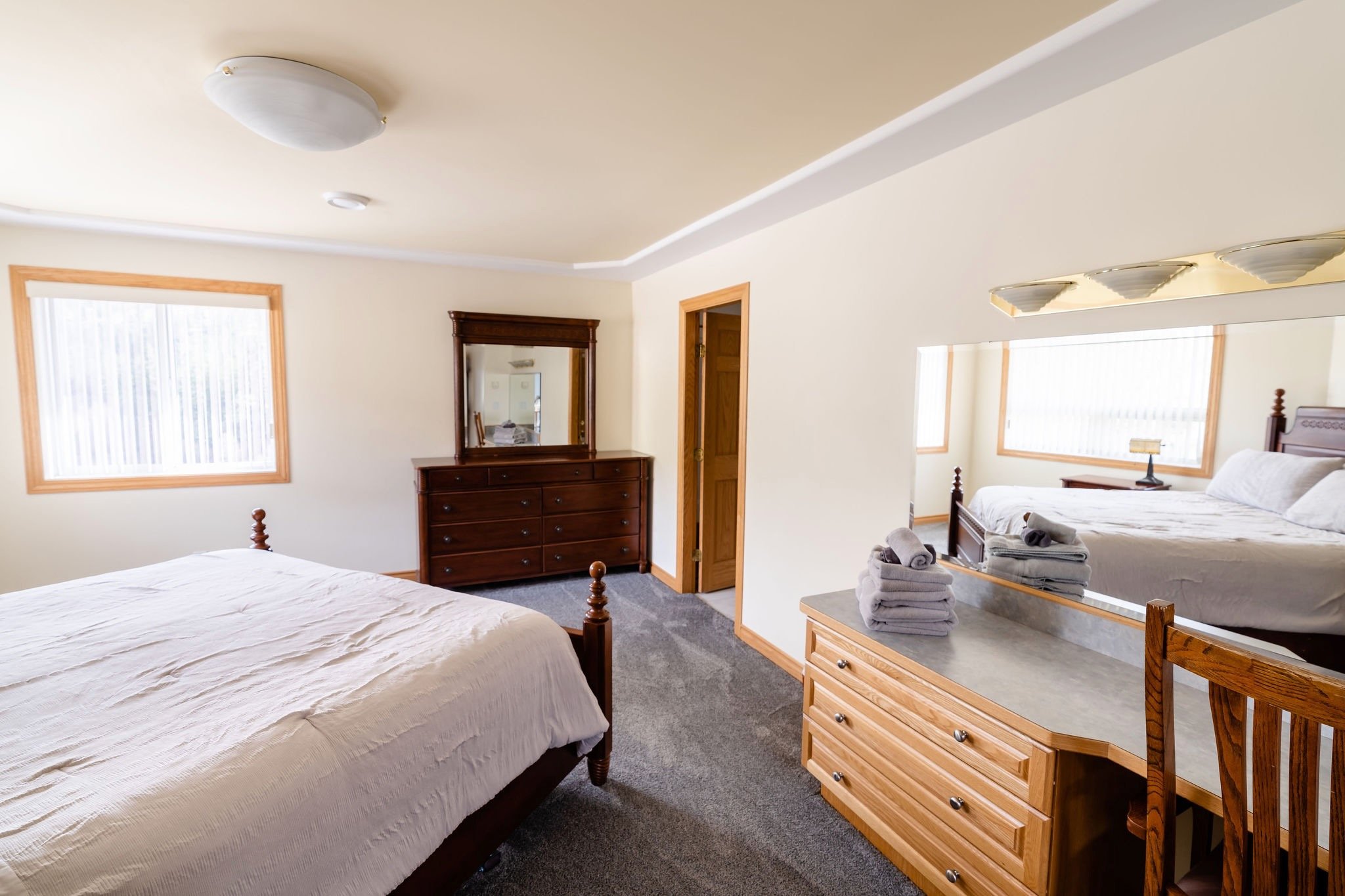 A bedroom with two beds, a dresser with a mirror, a wooden desk with a mirror, and a nightstand, all decorated in a traditional style with neutral colors.