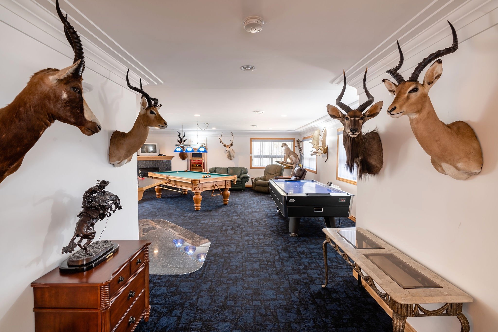 A game room with mounted animal heads on the wall, a pool table, and an air hockey table.