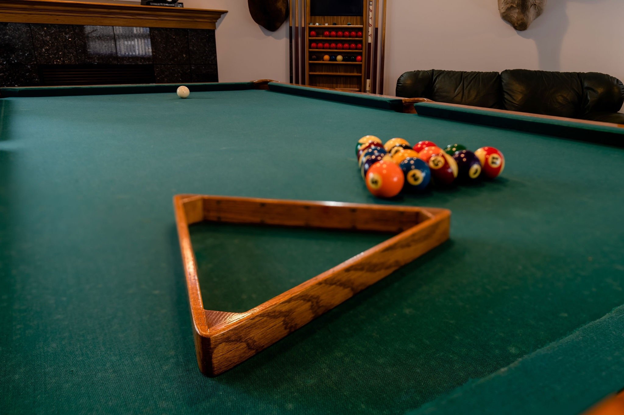 A pool table with a triangle rack and a cue ball, with a set of pool balls arranged in a formation, in a game room.