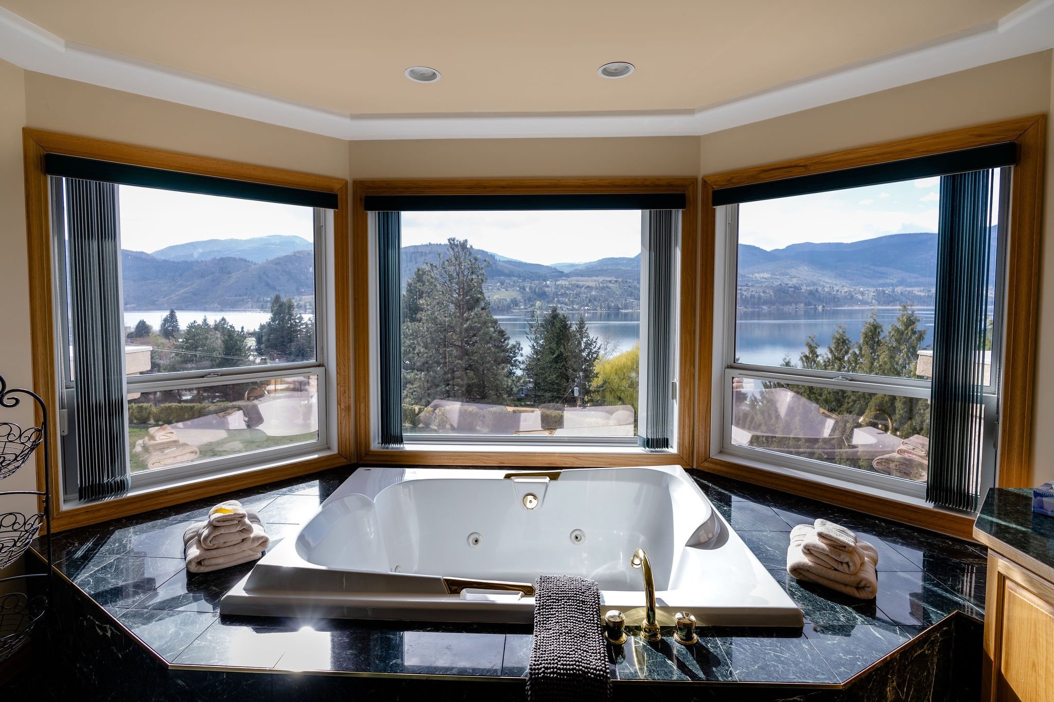 Luxury bathroom with a bathtub overlooking a lake and mountains through three large windows.