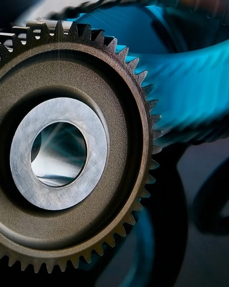 Close-up of a gear or sprocket with teeth, metal surface, and blue casing visible in the background.