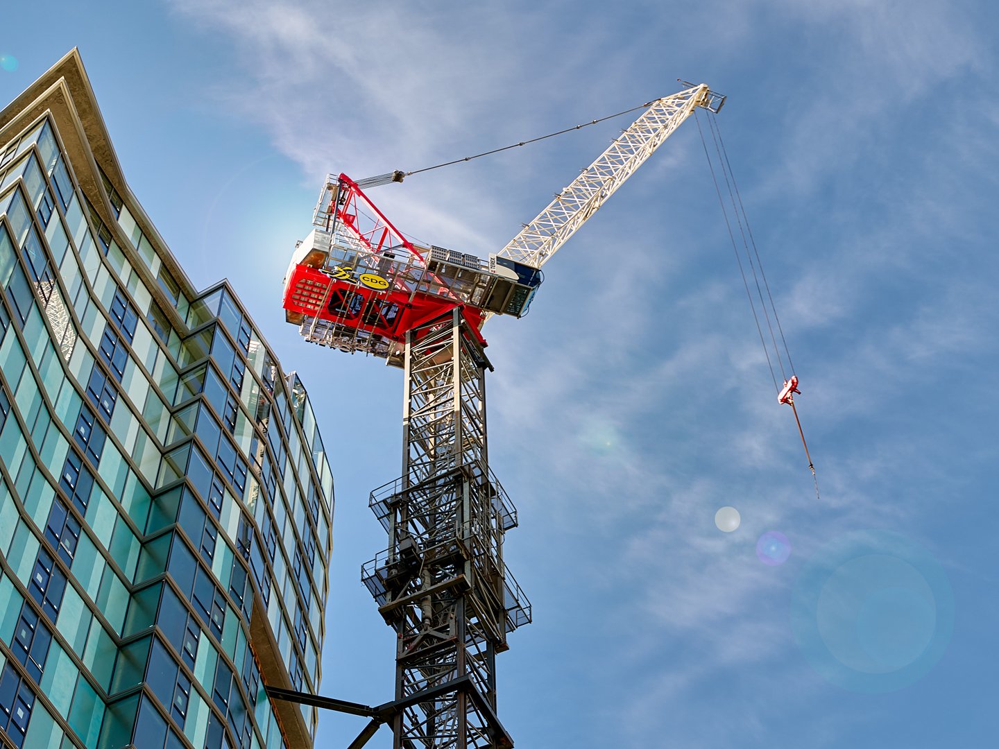 A construction crane next to a modern glass building against a blue sky with some clouds.