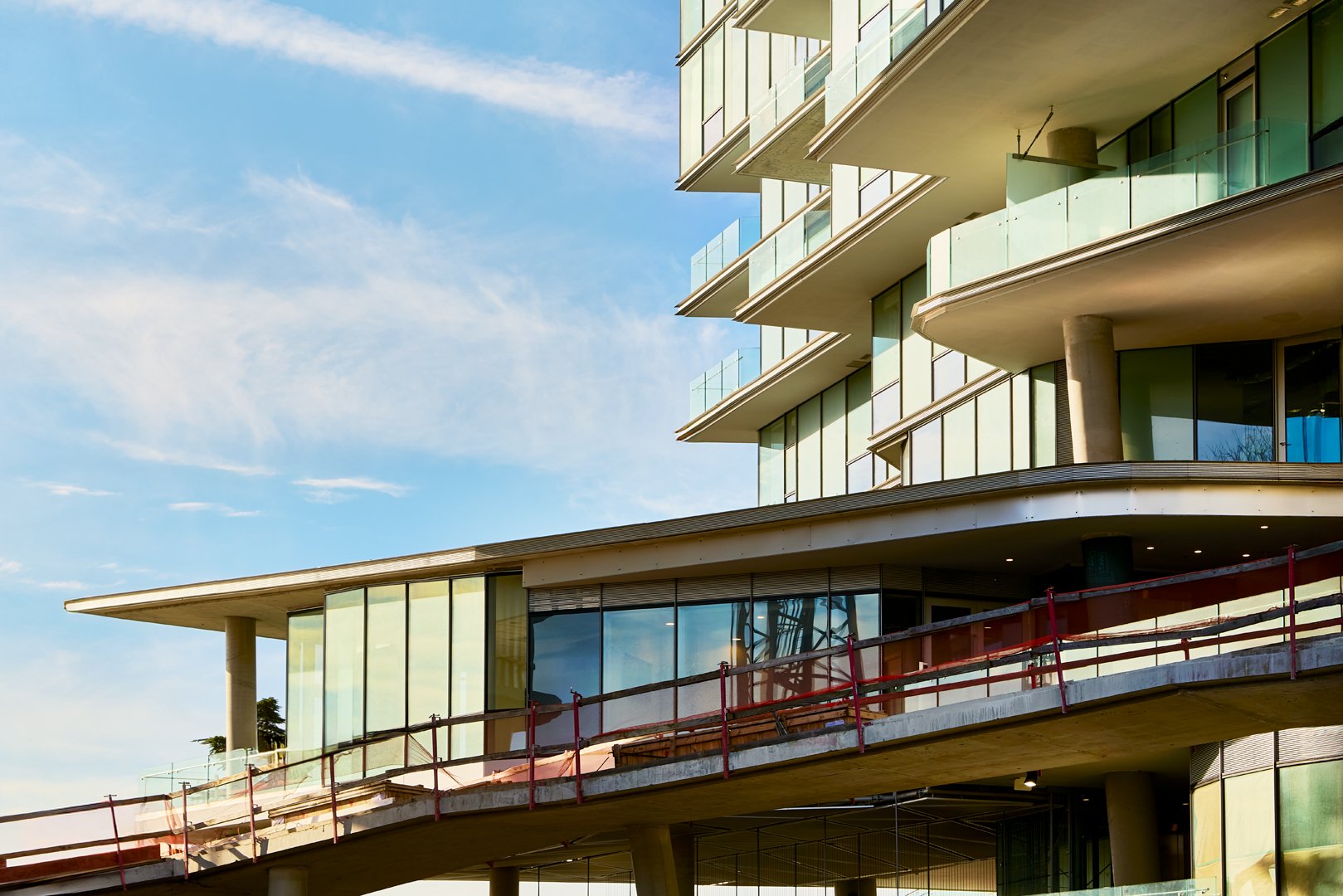 Modern multi-story building with glass windows and balconies against a blue sky.