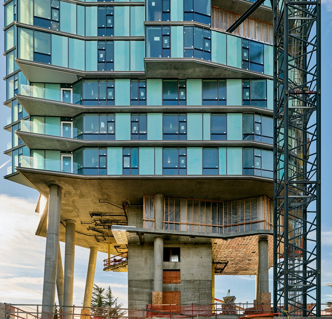 Modern multi-story building under construction with glass windows, concrete pillars, and construction equipment.