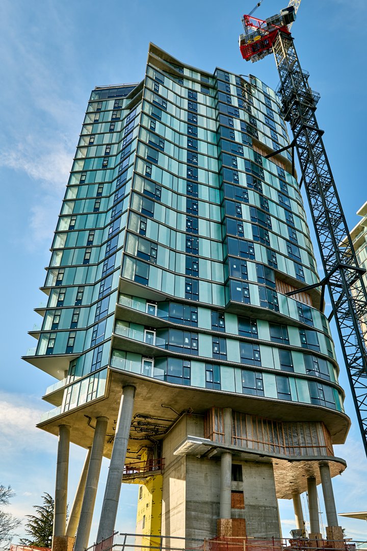 Modern high-rise building under construction with glass windows and a construction crane overhead.