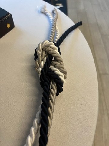 Close-up of a decorative three-strand rope knot in black, white, and gray on a table.