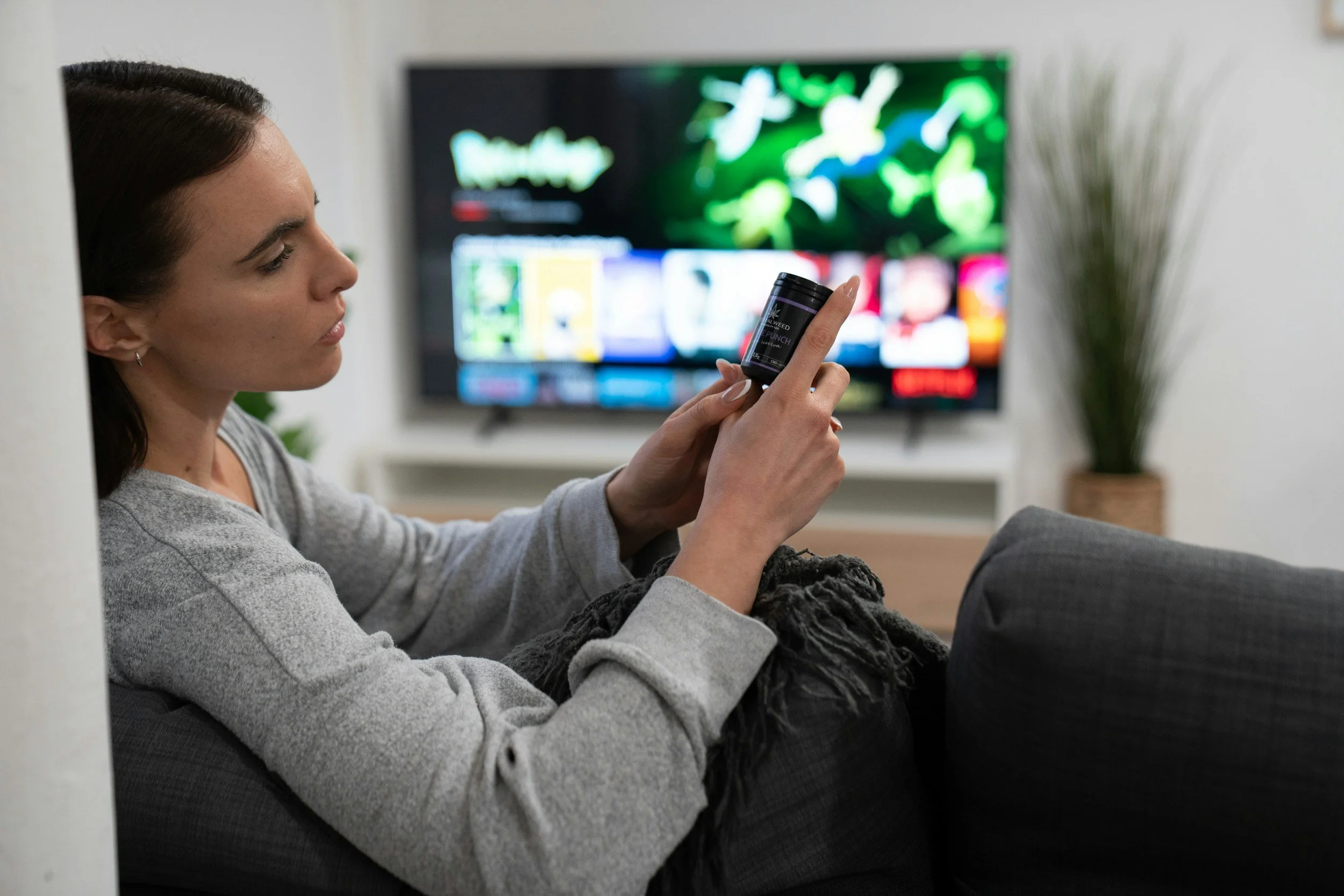 A woman looking at a cannabis bottle with the TV in the background