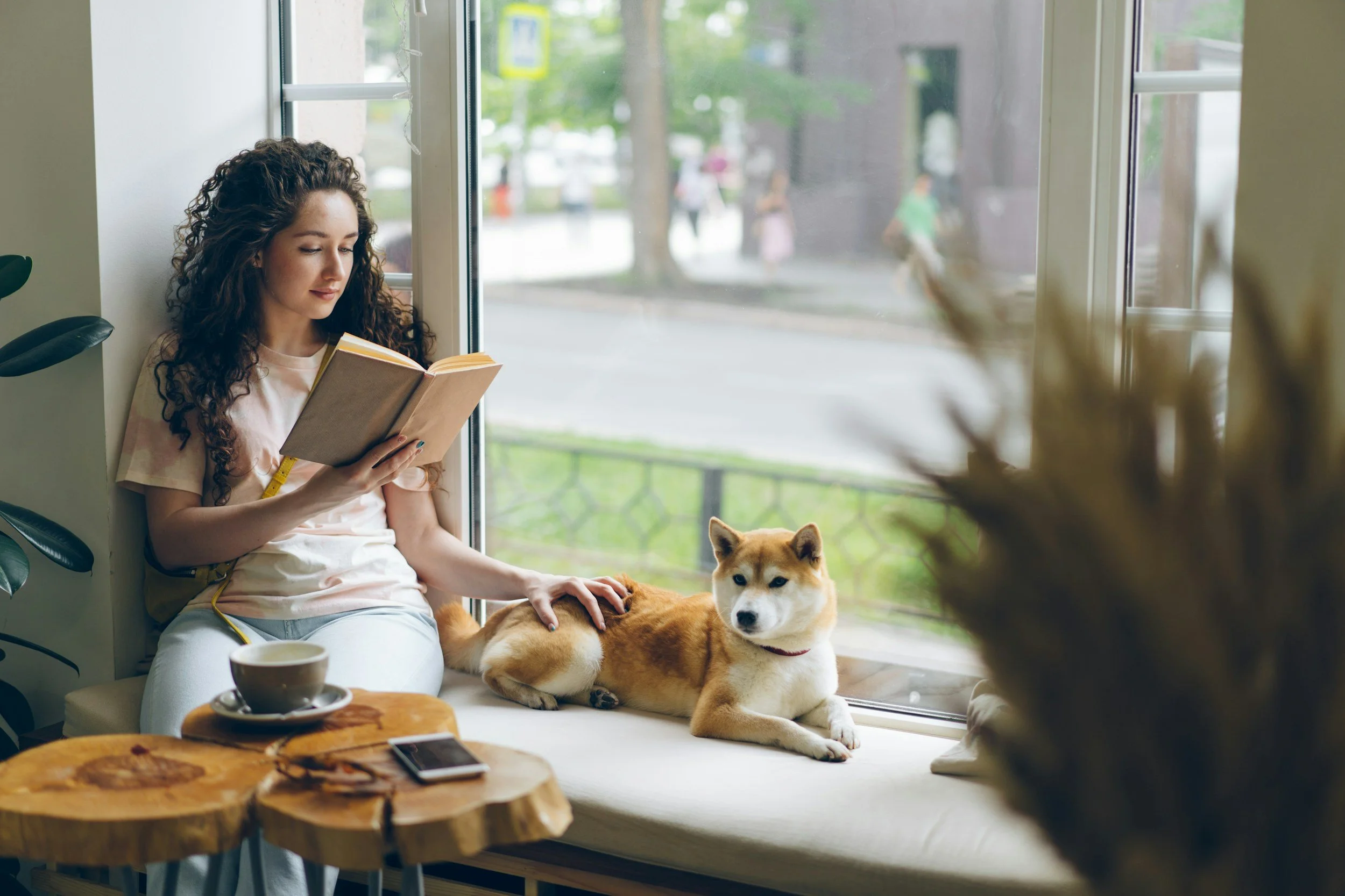 Woman reading a book while petting her dog with tea next to her