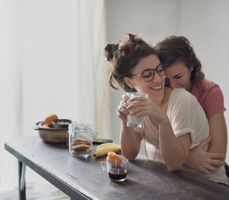 person hugging partner from behind in the kitchen over breakfast