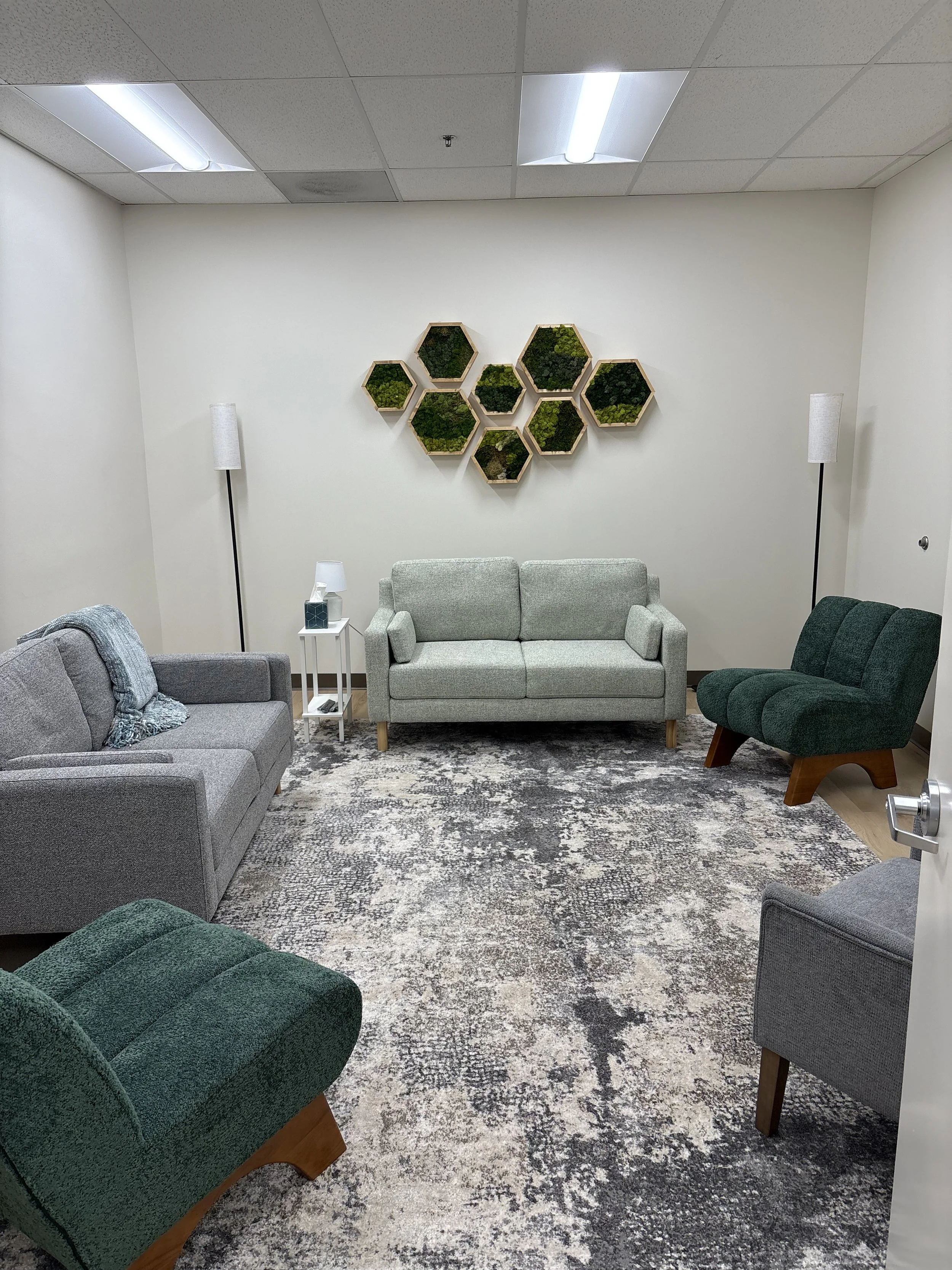 A waiting room with four couches and two floor lamps, with hexagon wall decor and a patterned rug.