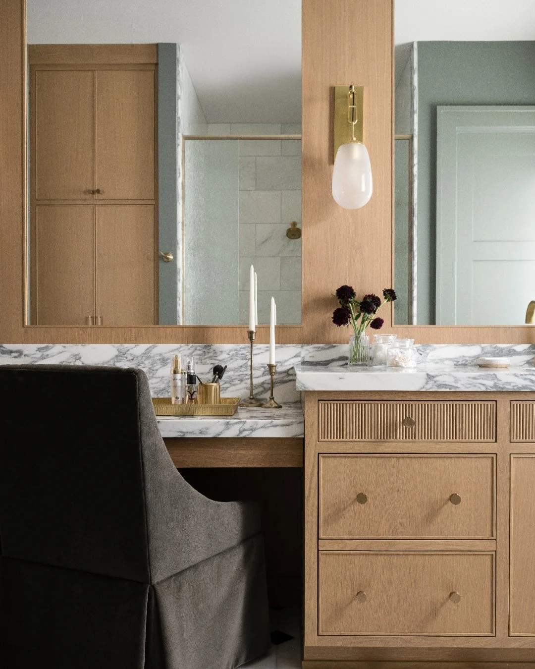 This primary bathroom was designed for shared living. The marble countertops set an elevated tone, paired with a custom his and hers vanity layout that keeps everything beautifully in place. The green velvet vanity chair adds a layer of elegance and 