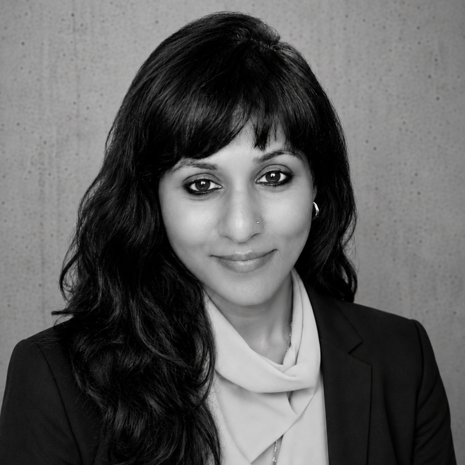 A grayscale image of a person wearing glasses and a striped shirt, leaning against a wall, looking directly at the camera.