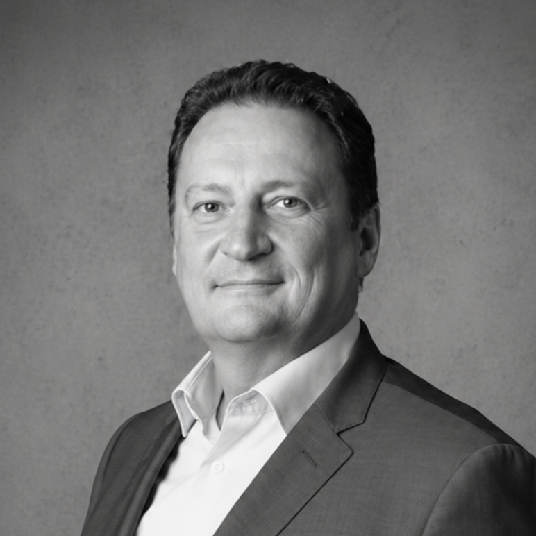 Black and white portrait of a man in glasses wearing a suit and striped shirt against a brick background.